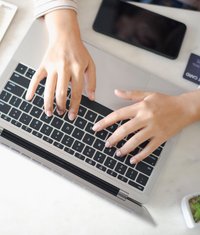 Zwei Hände tippen auf der Tatstatur eines Laptops